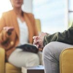 Close-up of two people sitting across from each other in a therapy or counseling session, with focus on hands and body language.