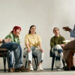 Group of people engaging in group therapy session led by therapist sitting in circle in cozy room with relaxed atmosphere, discussing personal issues and seeking support from each other